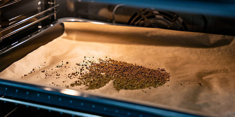 Macina Le Cime Di Cannabis Con Il Grinder Fino Ad Ottenere Una Consistenza Grossolana. Stendi I Frammenti Di Erba Su Una Teglia Con Carta Da Forno E Procedi Alla Loro Decarbossilazione In Forno Per 30–45 Minuti